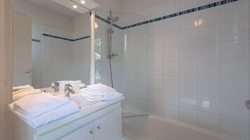 Een moderne badkamer met een douche met glazen wand, een wastafel met spiegel en een stapel witte handdoeken.