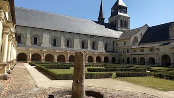 Pátio central com uma árvore, rodeado por um edifício com janelas em arco e uma torre.