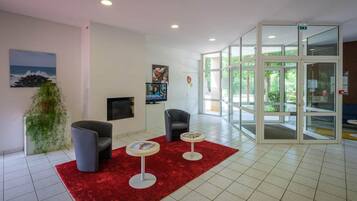 A modern lobby with a red carpet, two armchairs, a small table, a television, and a glass door leading outside.