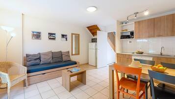 Un espacio habitable compacto con sofá, una mesa de comedor con sillas, una zona de cocina y una escalera.