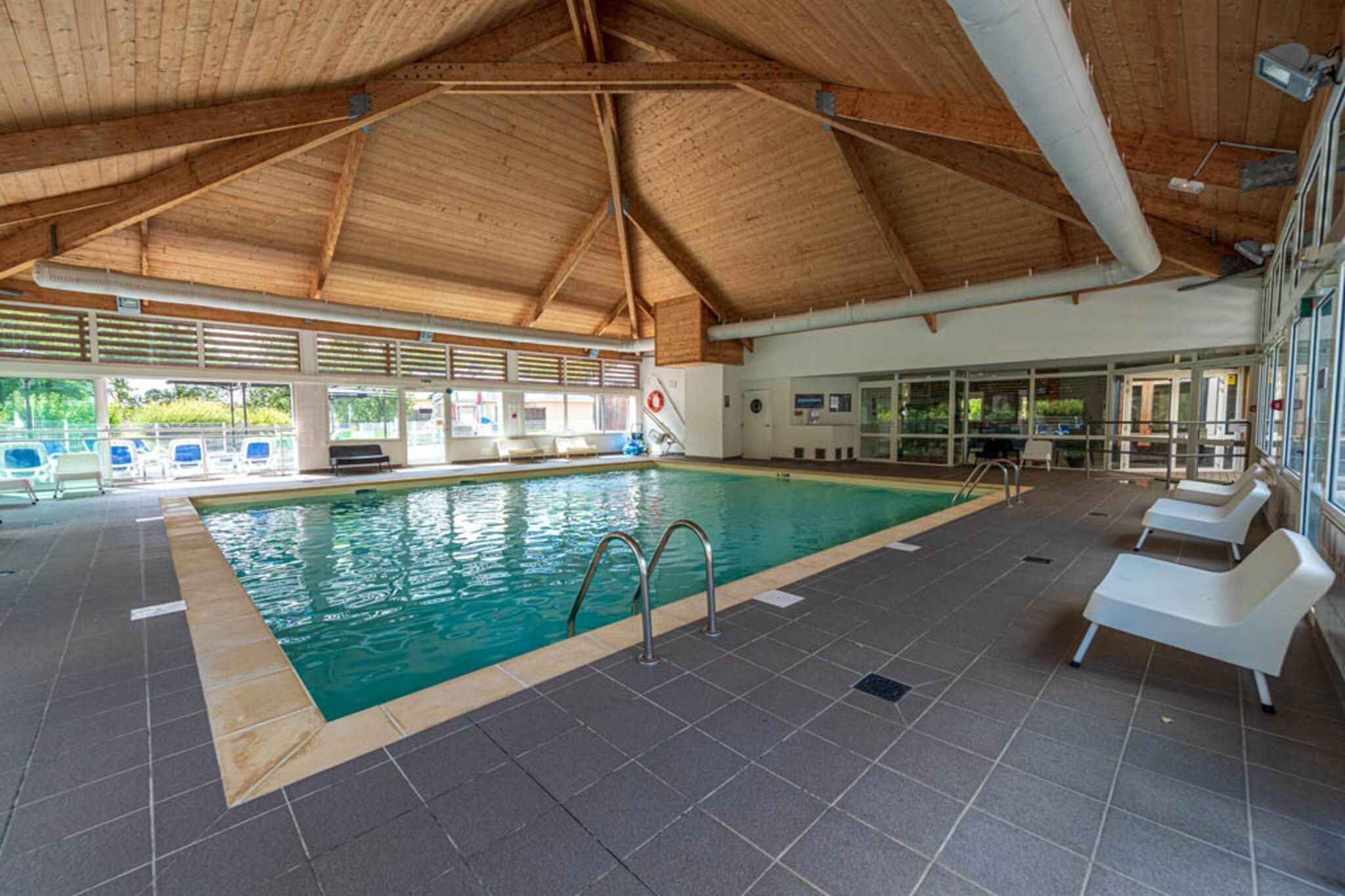 An indoor swimming pool with a tiled floor, a wooden ceiling, and a lifeguard chair.
