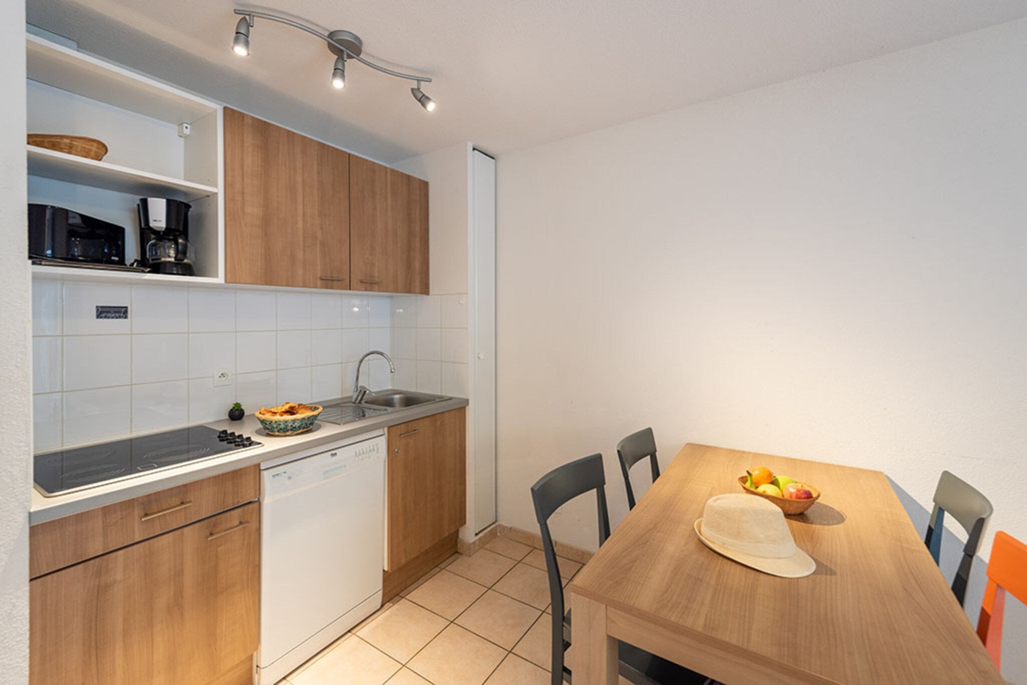 Una cocina compacta con lavavajillas, microondas y pileta. Hay una mesa de comedor con sillas y un tazón de frutas.