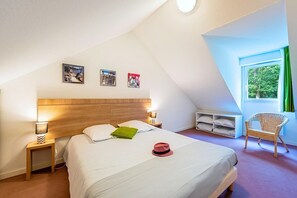 A bedroom with a bed, bedside tables, a chair, a window, and wall art.
