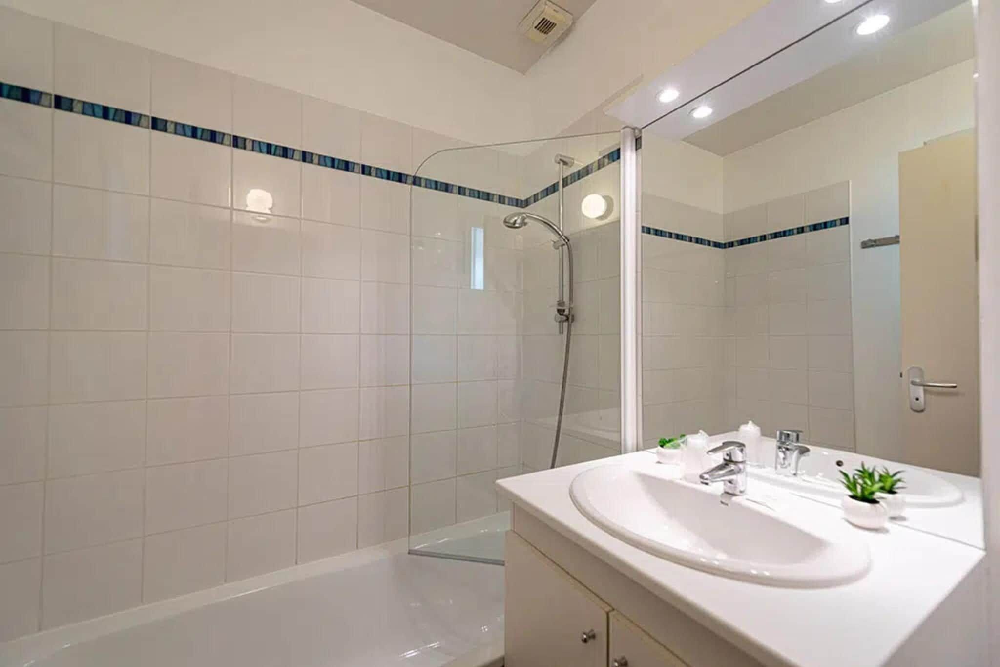 Een moderne badkamer met een douchecabine van glas, een witte wastafel met twee kraan en een grote spiegel.