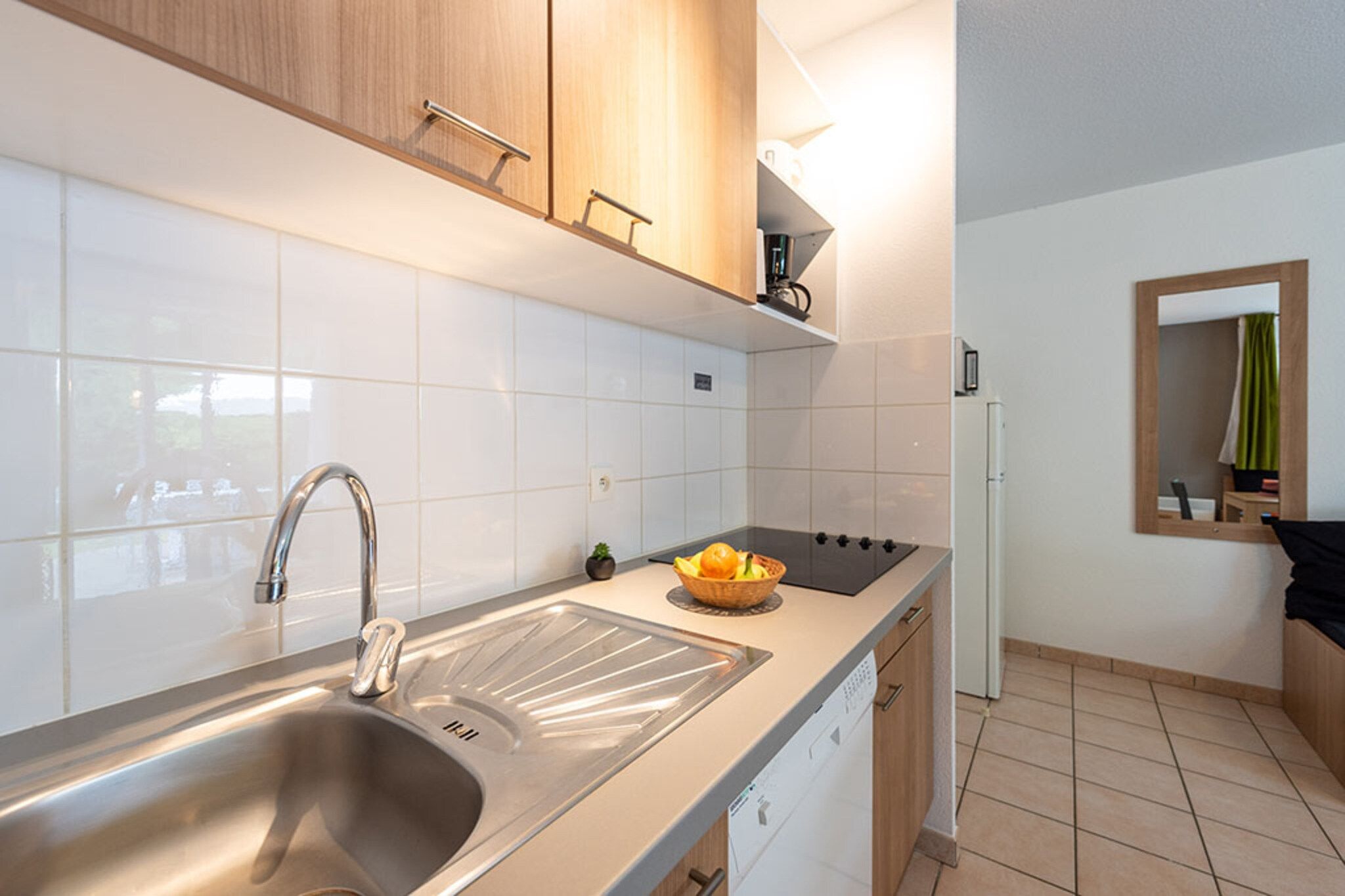 A modern kitchen with a stainless steel sink, a stove, and a bowl of fruit on the countertop.
