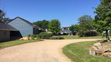 A residential driveway leading to a house with a blue exterior, surrounded by a well-maintained lawn and trees.