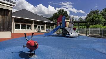 A playground with a slide and climbing structure, a red ball, and a building with large windows in the background.