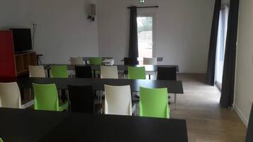 A conference room with tables and chairs, a television, and a window with curtains.