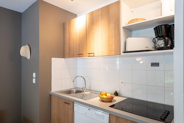 A compact kitchen with a dishwasher, a sink, and a coffee maker on the countertop.