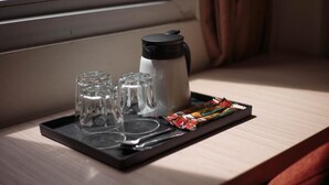 Un vassoio con un thermos, posacenere per sale e pepe e una confezione di snack su un piano di legno vicino a una finestra.