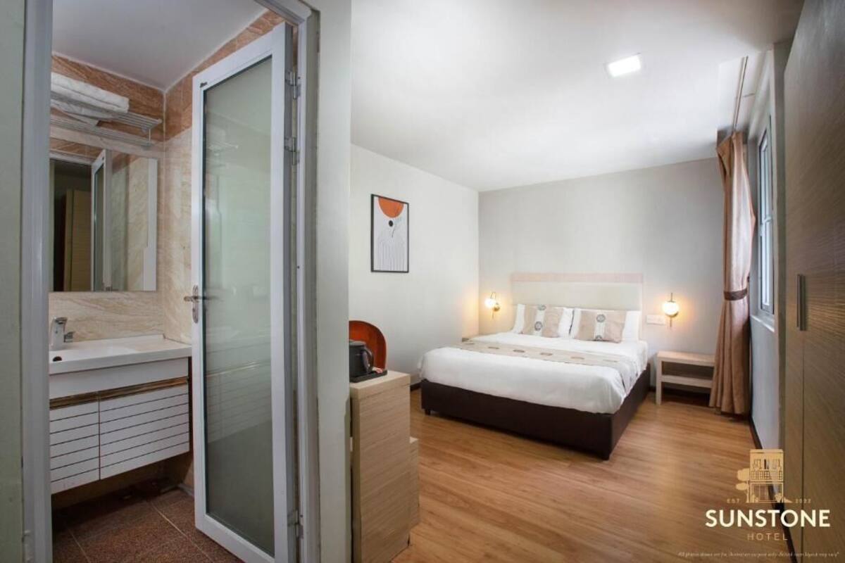 Une chambre d’hôtel comprenant un lit, une table de chevet, une lampe et une salle de bain avec un lavabo et un miroir.