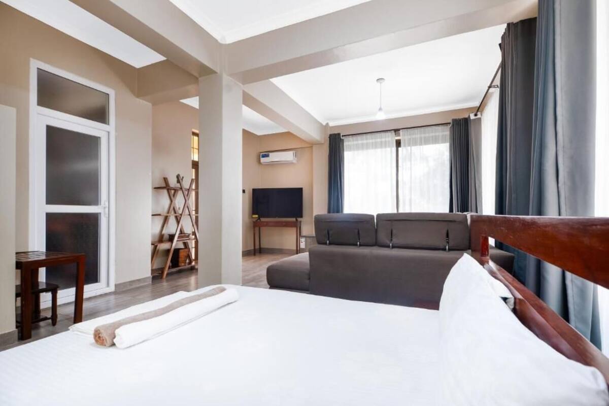 A hotel room with a bed, a sofa, a TV, and a window with curtains.