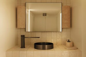 Ein modernes Badezimmer mit einem wandmontierten Waschbecken, einem runden Becken und einem Handtuchspender.