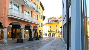 Eine Kopfsteinpflasterstraße, gesäumt von mehrstöckigen Gebäuden, einige mit Balkonen und Schaufenstern.