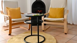 Ein Zimmer mit zwei Sesseln, einem kleinen Tisch, einem schwarzen Kamin und einem gelben Teppich.