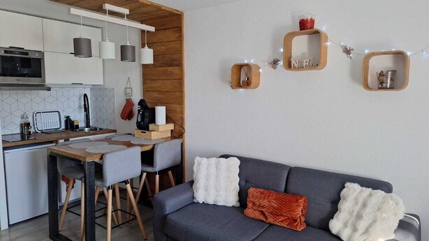 A modern kitchen with a built-in oven, a dining area with a wooden table and chairs, and a grey sofa with decorative pillows. - La parenthese suspendu (Font-Romeu-Odeillo-Via)
