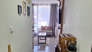 A narrow hallway leading to a living room with a sofa, a wooden shelf with a figurine, and framed pictures on the wall. - La parenthese suspendu (Font-Romeu-Odeillo-Via)