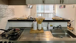 Una cocina con armarios de madera clara, estufa a gas, un lavabo y una ventana con persianas.