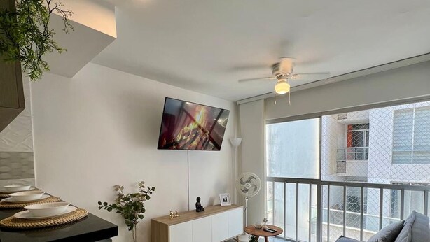 Una sala de estar moderna con televisor de pantalla plana, un sofá, un comedor con mesa y un balcón con vistas.