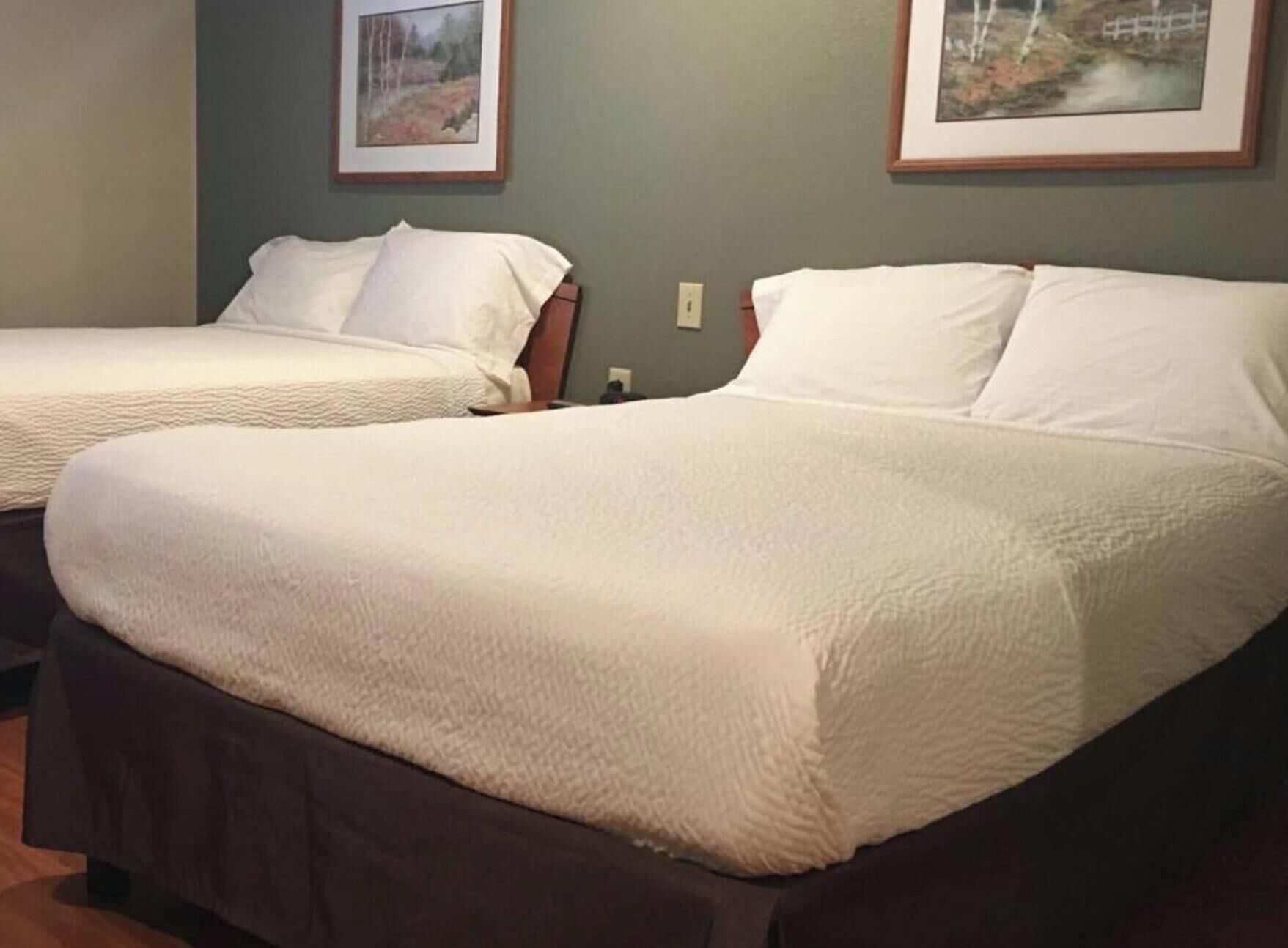 Two twin beds with white bedding, a wooden headboard, and a framed picture on the wall.