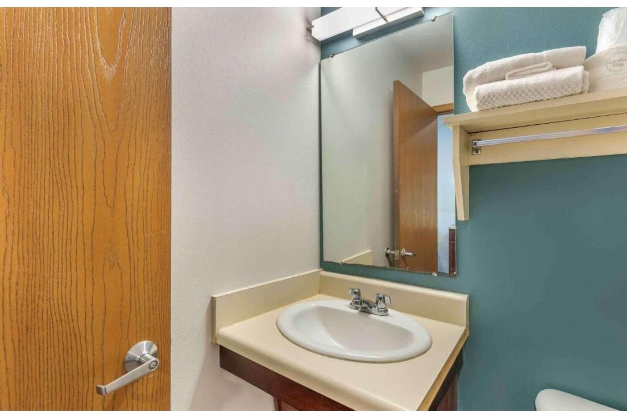 A bathroom with a sink, mirror, towel rack, and wooden door.