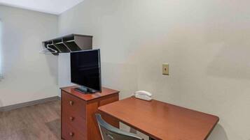 Une petite pièce simple, avec un bureau, une chaise, un téléviseur posé sur un meuble en bois et un téléphone.