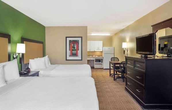 A hotel room with two beds, a kitchenette, a desk, a television, and a dresser.