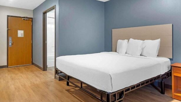 A hotel room with a bed, a wooden floor, a blue wall, and a door. - ADA Full Bed,Tub,Nsmk|Kitchen|Studio 6 Fort Myers (Fort Myers FL)