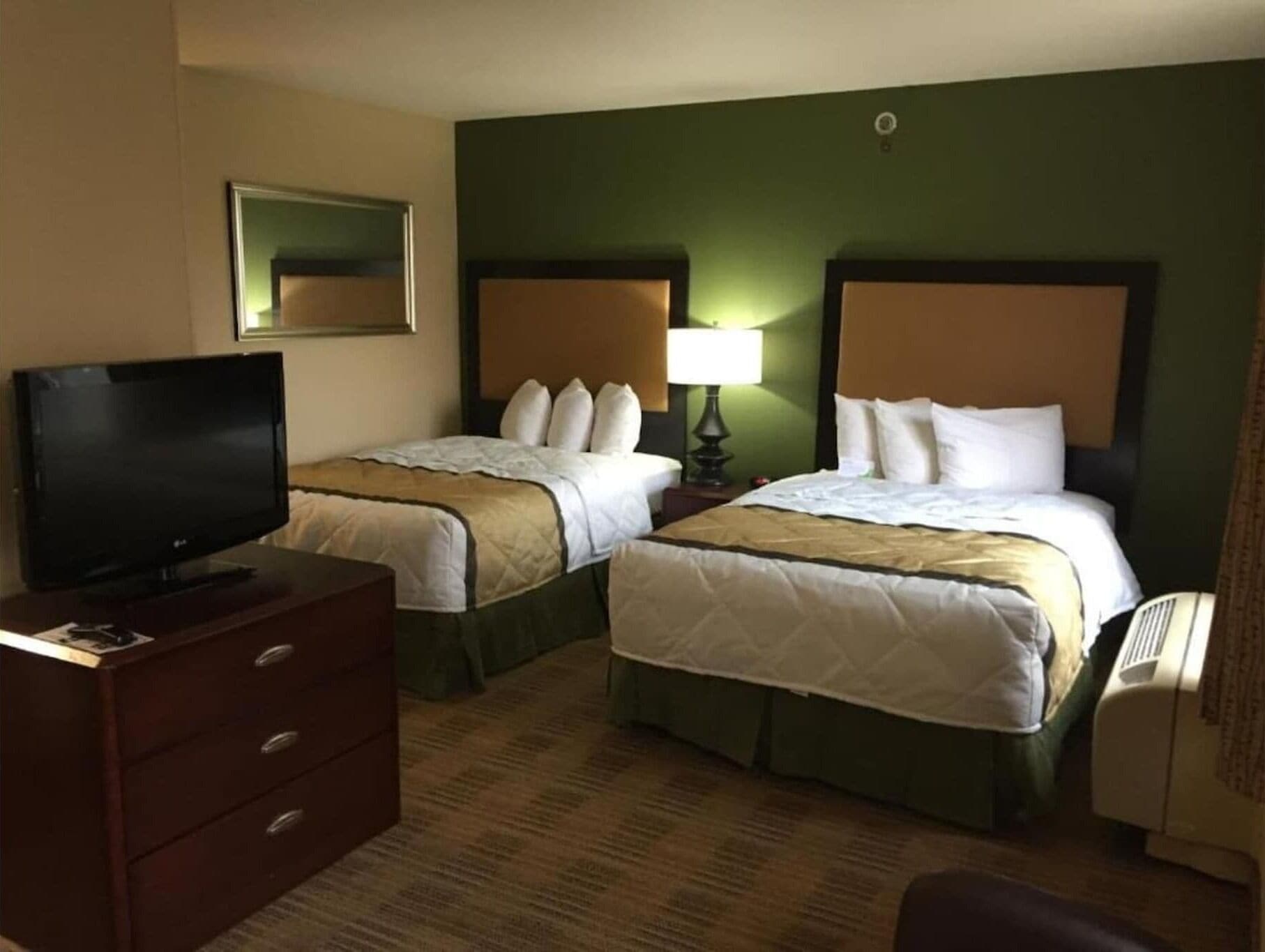 A hotel room with two beds, a TV, a dresser, and a lamp.
