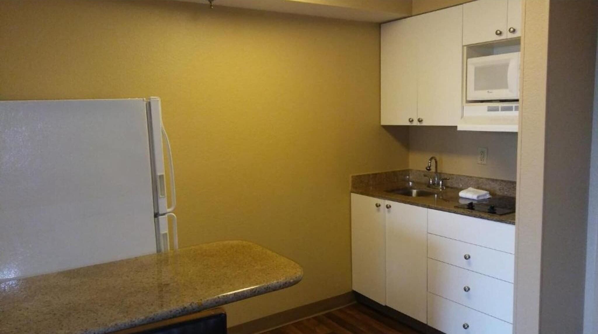 Eine kleine Küche mit Kühlschrank, Mikrowelle, Spüle und einer Arbeitsplatte aus Granit.