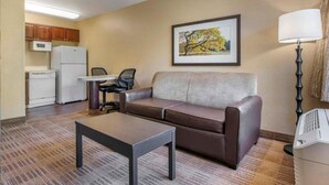A compact living space with a sofa, a small table, a kitchenette, and a framed picture on the wall.