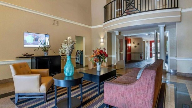 A lobby with a sofa, armchairs, a coffee table, a TV, and a vase with flowers.