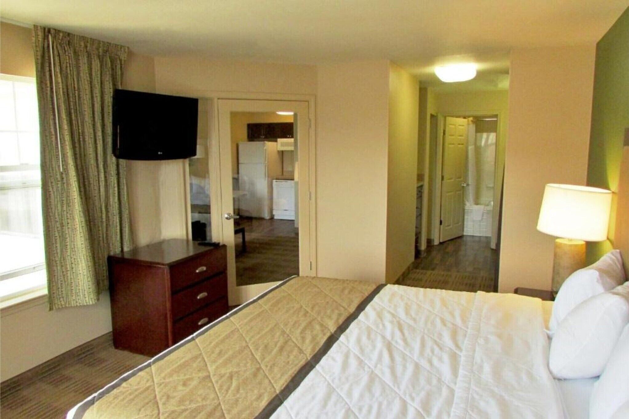 Ein Hotelzimmer mit Bett, Kommode, Fernseher und Spiegel.
