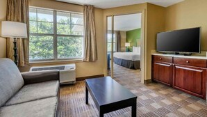 Habitación de hotel con sofá, televisor, escritorio, cama y vista a zonas verdes.