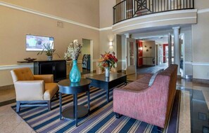 A hotel lobby with a sofa, chairs, a coffee table, a TV, and a vase with flowers.