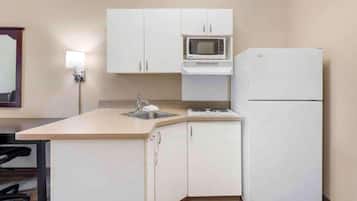 A compact kitchen with white cabinets, a microwave, a refrigerator, and a sink.