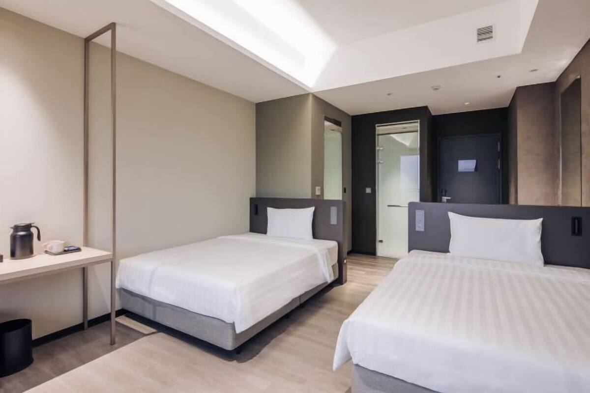 A modern hotel room with two beds, a desk, and a large mirror.