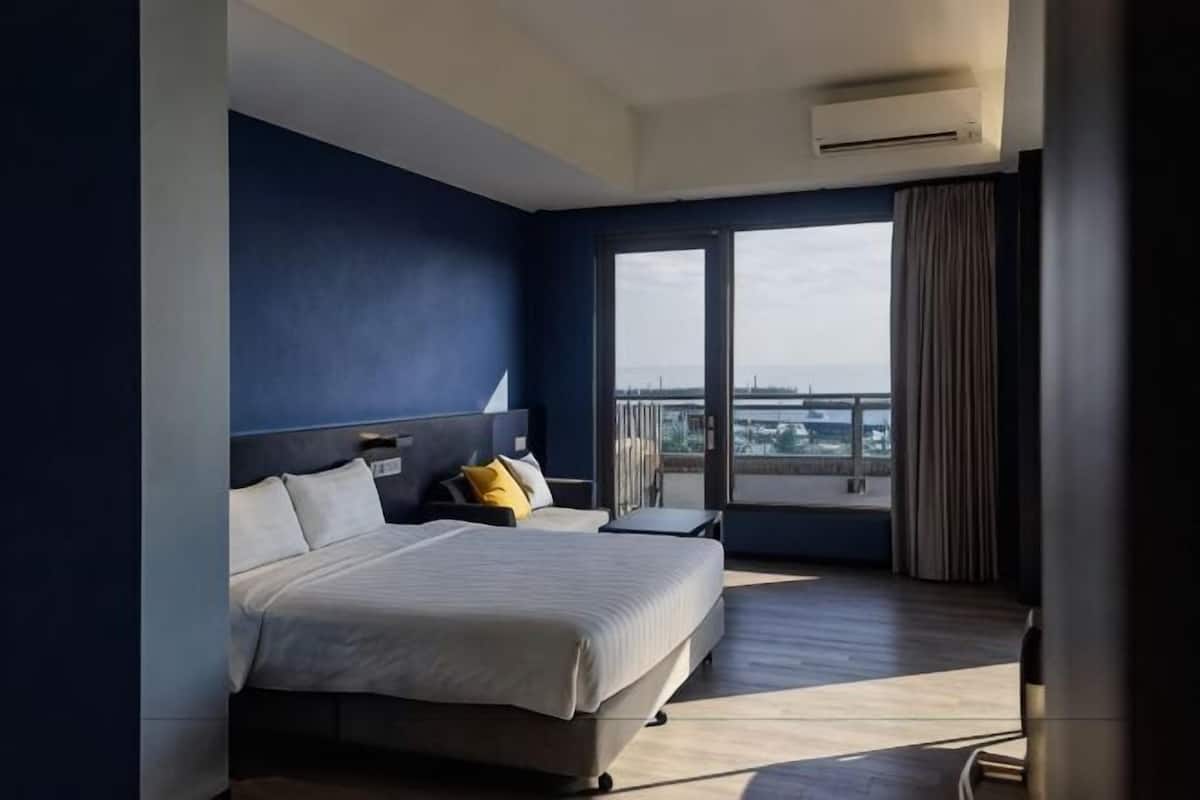 A hotel room with a large bed, a nightstand, a desk, and a view of the city.