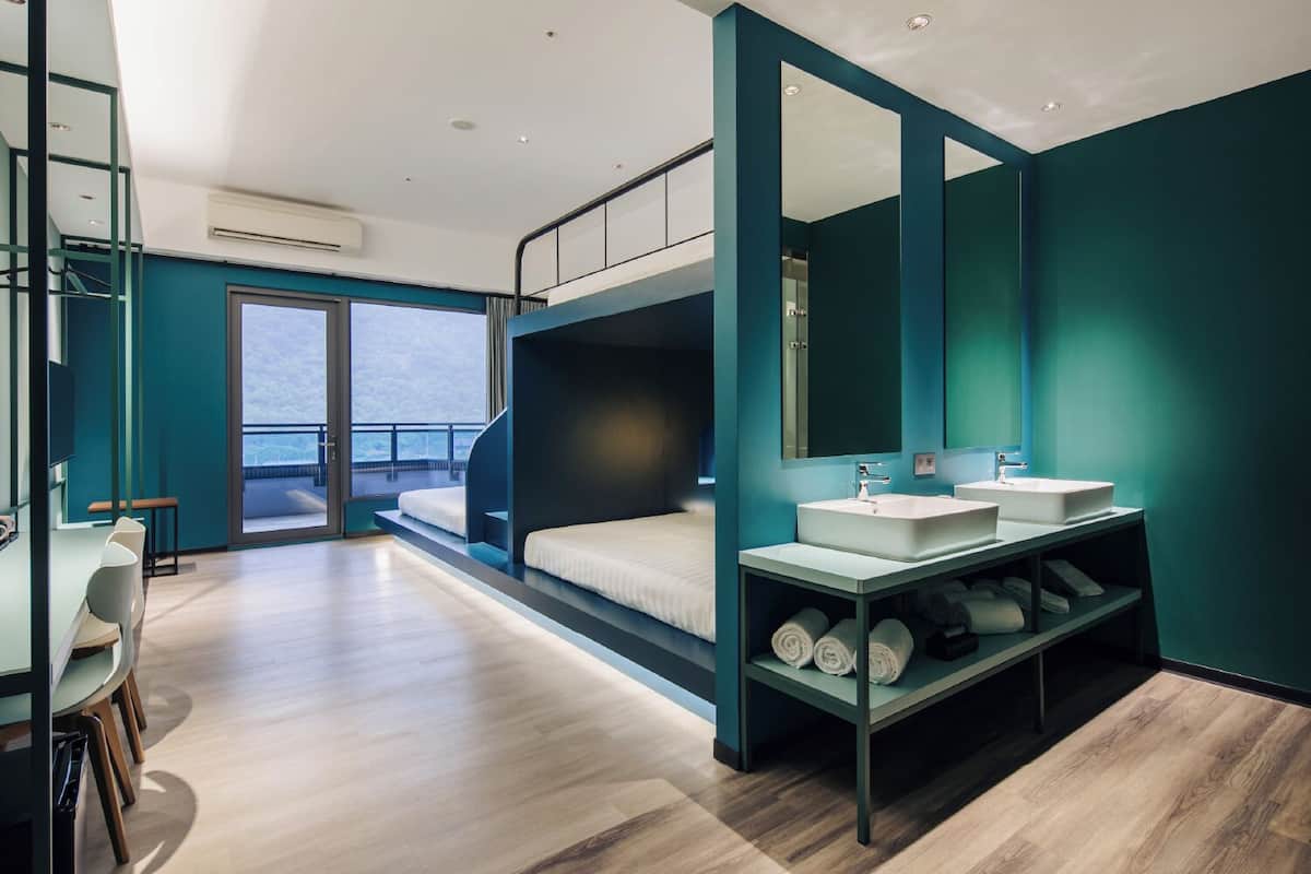 A modern room with a bunk bed, a desk, a mirror, and a bathroom with a sink and towel rack.