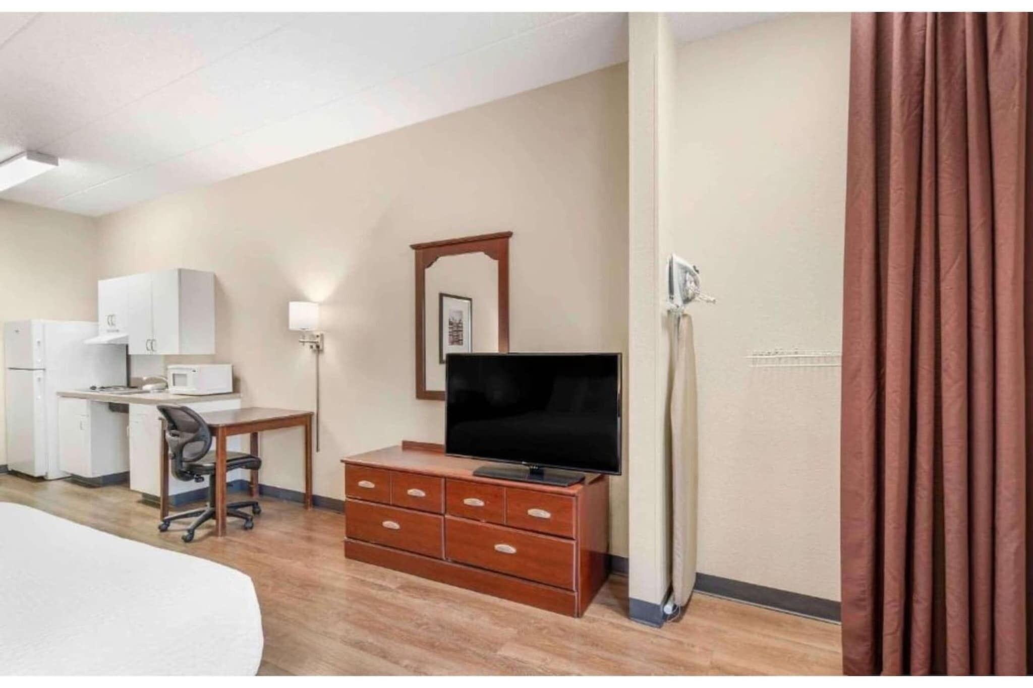 Ett hotellrum med en säng, ett skrivbord med en dator, en tv, en byrå och en mikrovågsugn.