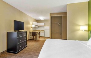 Habitación de hotel con cama, escritorio, televisión, armario y ducha.