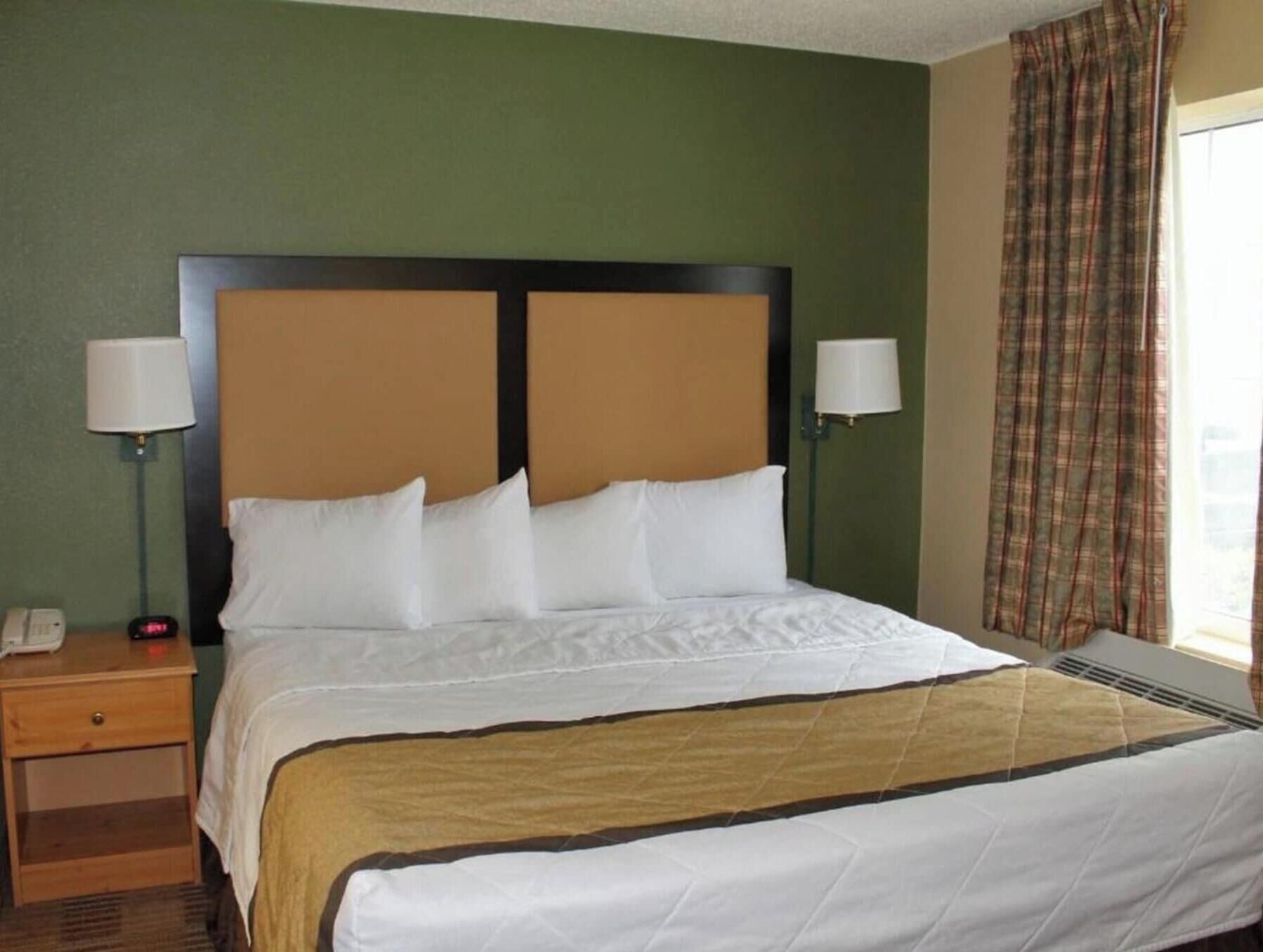Habitación de hotel con cama, dos lámparas de noche, mesita auxiliar, teléfono y ventana con cortinas.