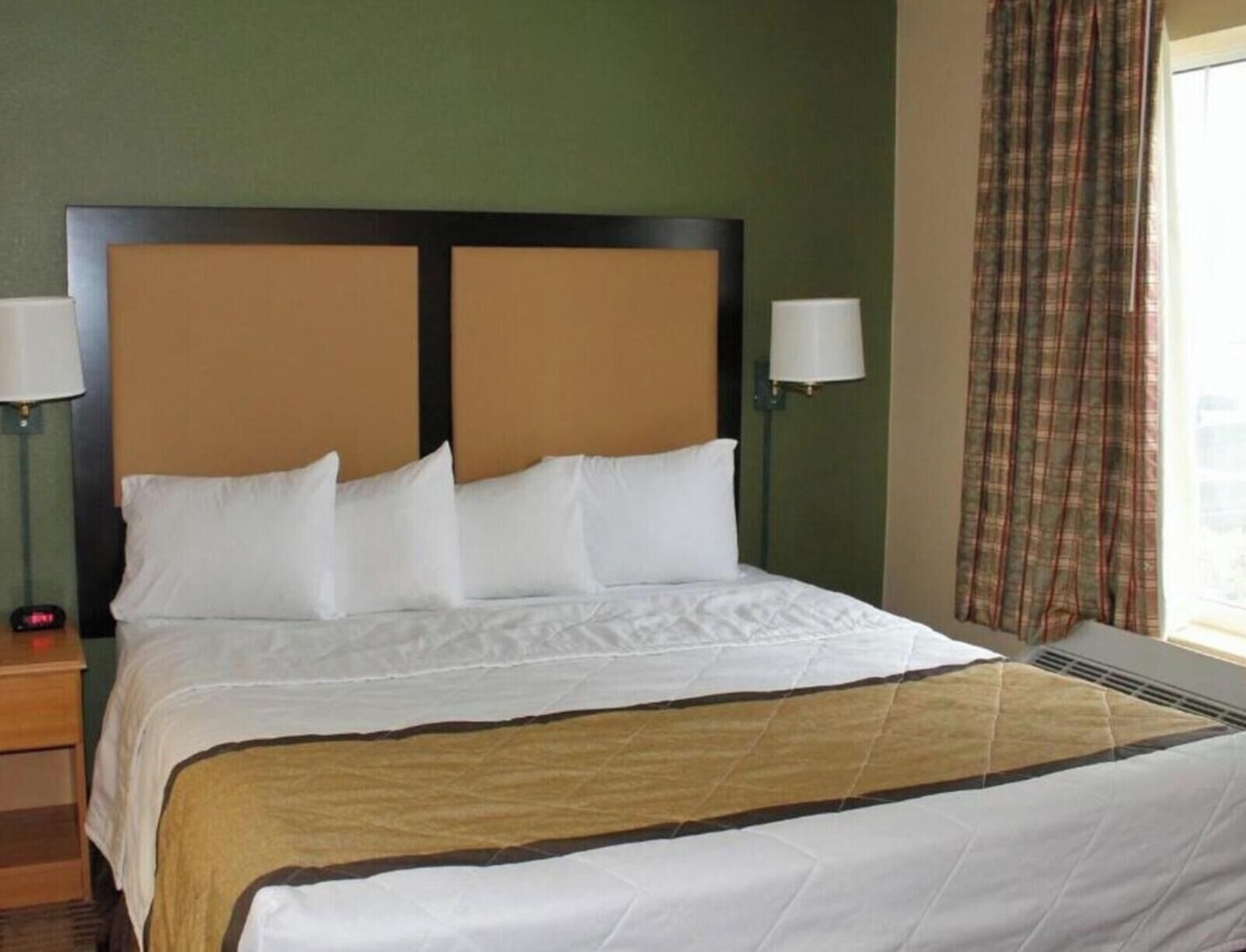 Une chambre d’hôtel avec un grand lit, deux lampes de chevet, une tête de lit et une fenêtre avec des rideaux.