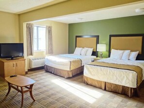A hotel room with two beds, a television, a small table, and a window with curtains.