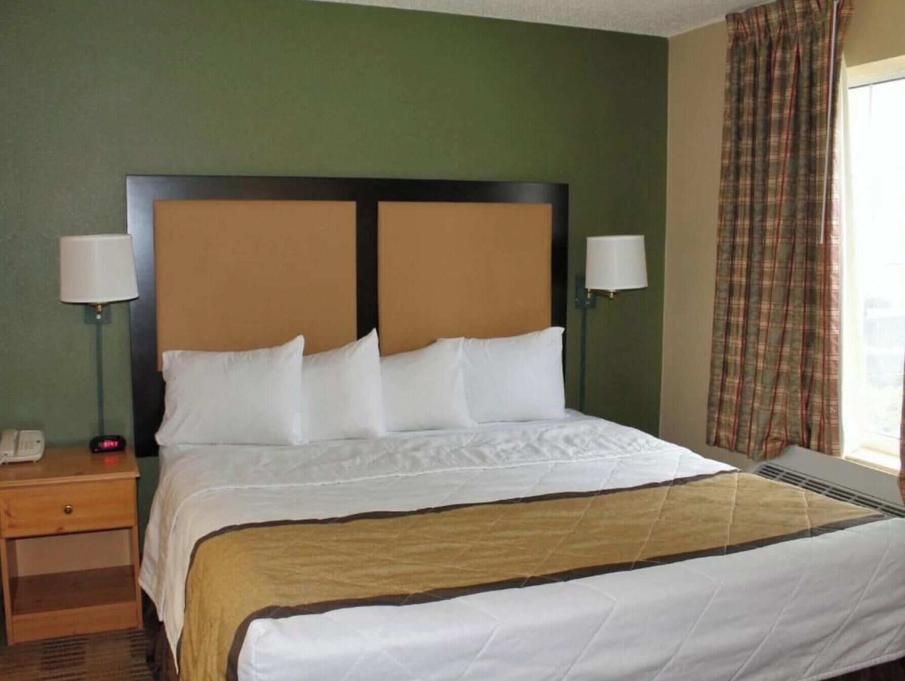 Habitación de hotel con cama, dos lámparas de noche, mesita auxiliar, teléfono y ventana con cortinas.