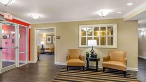 A hotel lobby with a striped carpet, two leather armchairs, a small table with a lamp, and a large window. - 1 King Bed | Non-Smoking, Kitchen, Shower (Chicago)