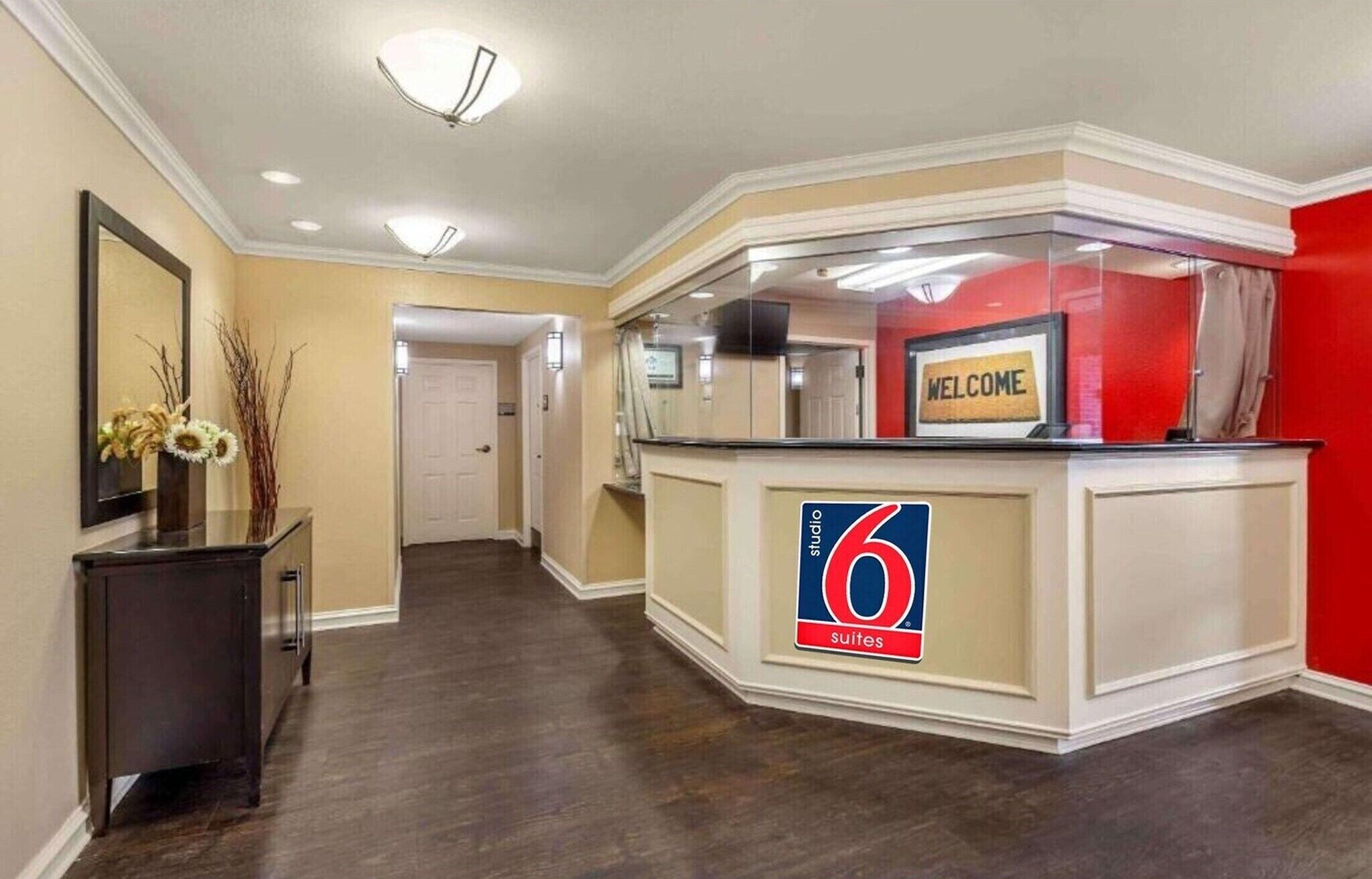 A hotel reception area with a '6 suites' sign, a 'WELCOME' sign, and a hallway leading to a door.