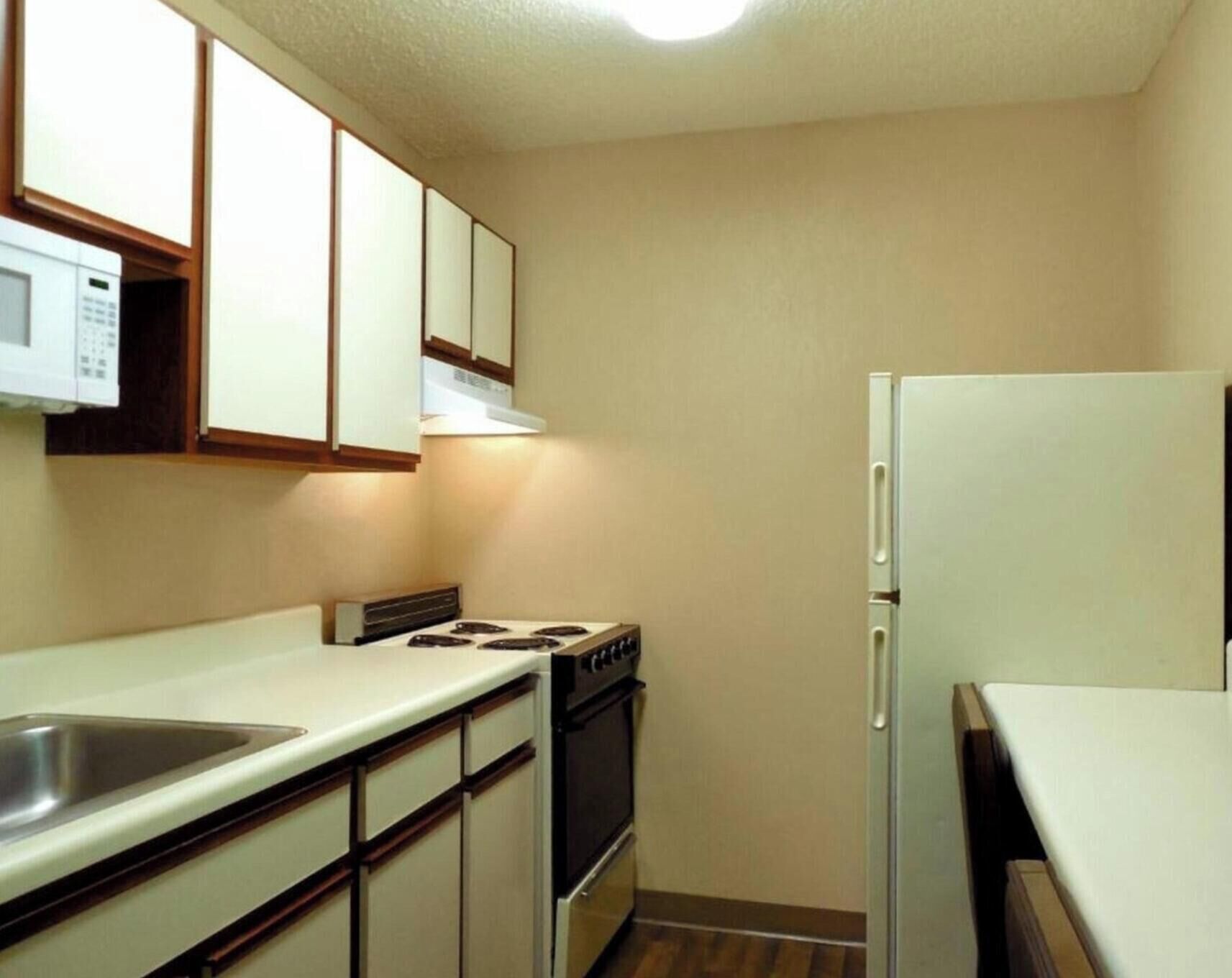 A compact kitchen with a stove, oven, and refrigerator, featuring wooden cabinets and a white countertop.
