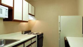 A compact kitchen with a stove, oven, and refrigerator, featuring wooden cabinets and a white countertop.