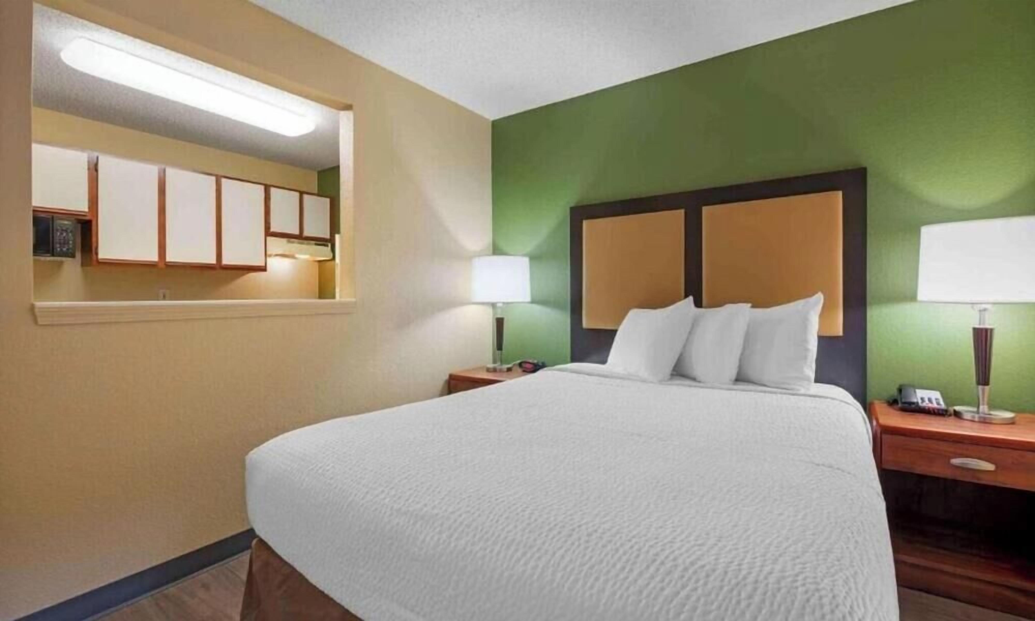 A hotel room with a large bed, two bedside tables, a nightstand, a mirror, and a green accent wall.